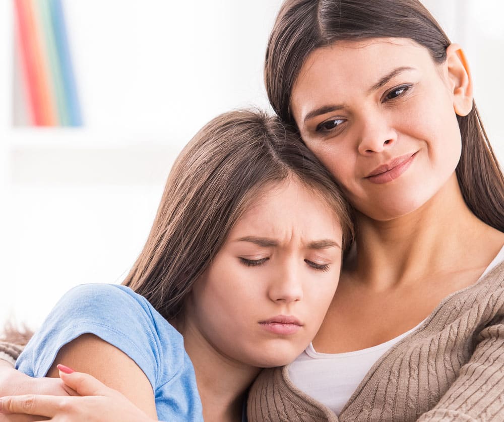 Closed up photo of teen girl comforted by their mother