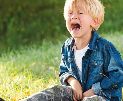 Closed up photo of young boy in a grass field crying