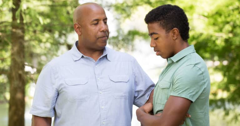 A concerned adult gently talks to a teen who appears upset, illustrating the importance of supportive conversations when considering teletherapy for teens.